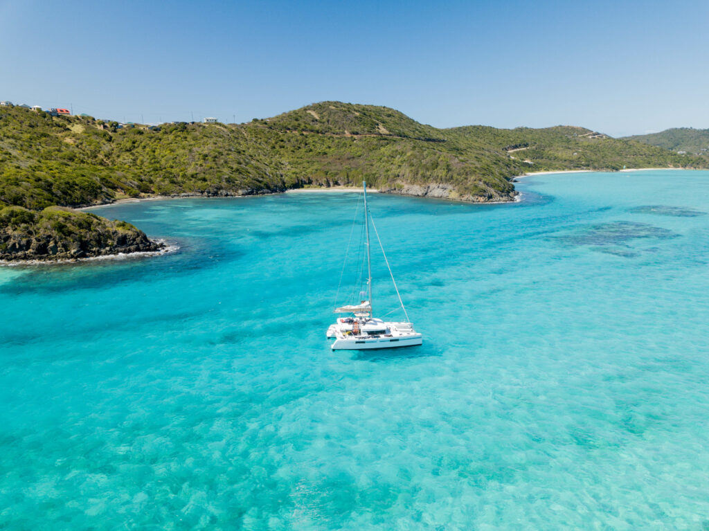 Catamaran in the Caribbean blue waters of a lush green island